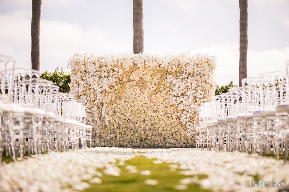 White rose flower wall decorated with a carpet of white rose petals, with white chairs placed on either side of the wedding ceremony aisle at the Park Hyatt Aviara resort in Carlsbad, California