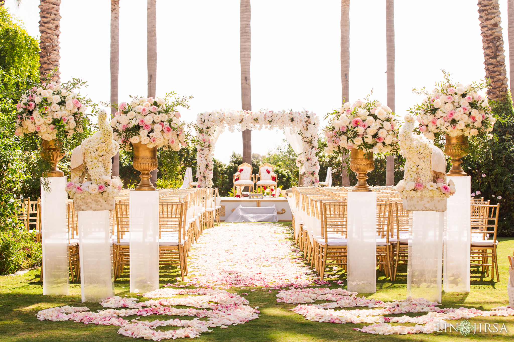 Lavish wedding altar with straw colored chairs and white rose petals carpeting the bridge and groom walkway, under palm trees in Carlsbad, California at the Park Hyatt Aviara Resort