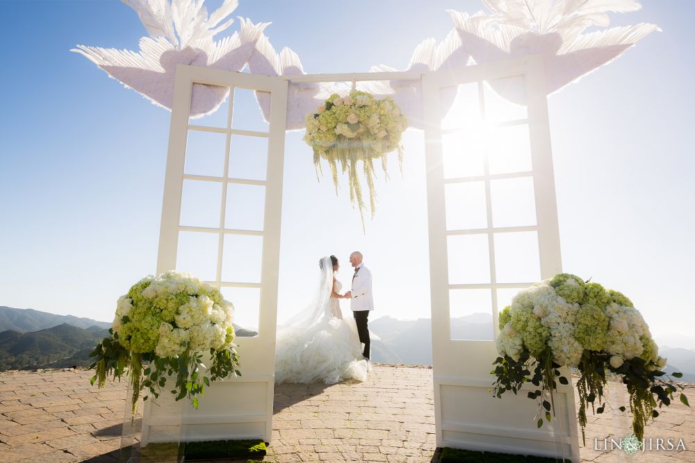 A Caucasian couple getting married in a simple wedding ceremony at Malibu Rocky Oaks Estate with the Appalachian mountains in the background and white doves, flying over the marble white wedding altar Nondenominational wedding ceremony photographed by Lin and Jirsa at the Malibu Rocky Oaks Estate in Southern California