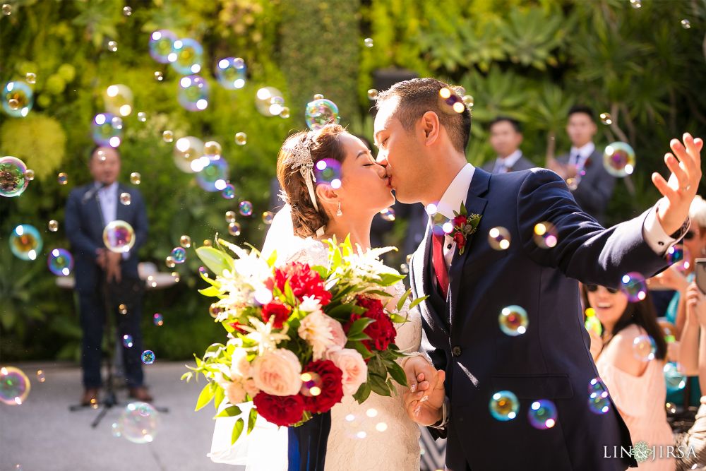 Lin and Jirsa photographing a Chinese wedding in front of the Grand Exit Smog Shoppe in Los Angeles with Orange Blossom Events at 2651 S La Cienega Blvd, Los Angeles, CA 90034 A Chinese couple kissing and getting married with bubbles gently floating above, set against a green forest background