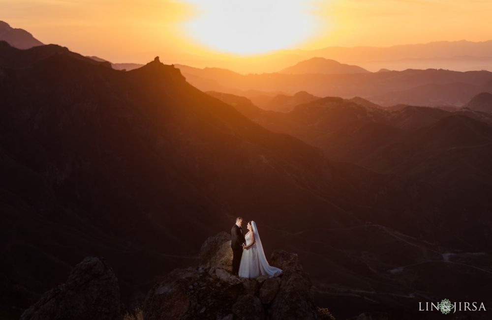 Lin and Jirsa photograph a wedding couple during sunset in the mountains, perched on a rocky outcrop with orange hues saturating the background