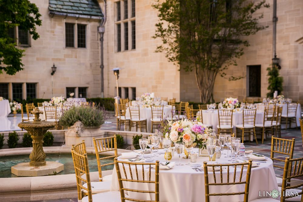 Pink tables with elegant brass chairs with a water fountain in the background, in front of the Greystone Mansion, located in Beverly Hills, California