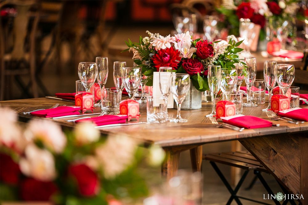 Elegant Chinese wedding reception decor shot by Lin and Jirsa Los Angeles Wedding Photography with Orange Blossom Special Events Beautiful red and pink carnation and rose flower bouquets on a rustic wooden table with silverware and bright pink cloth napkins